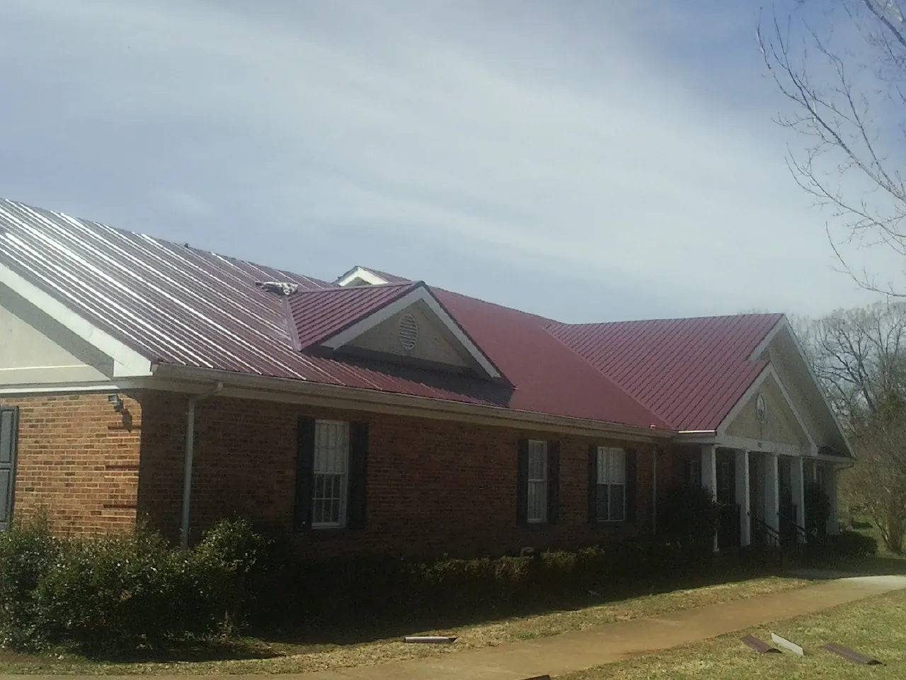 Red metal roof with gabled entries on a long brick building, from a Hail Damage Roof Repair job in South Windsor