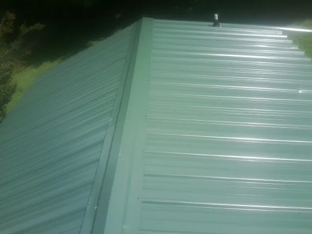New green metal panels meeting at the ridge of a roof — Flat Roof Repair work by our crew in South Windsor