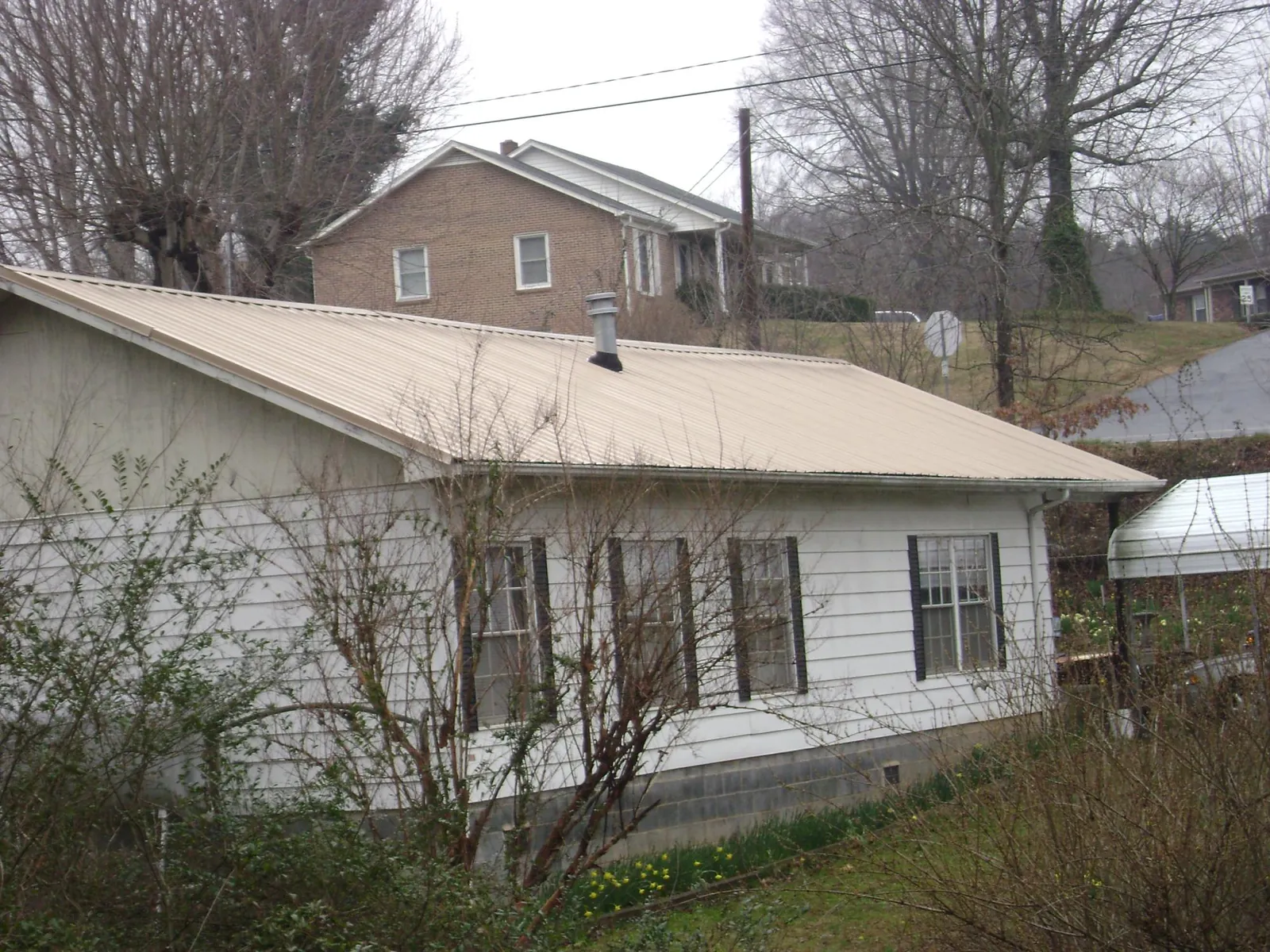 Tan metal roof on a white sided house set into a hillside — Commercial Roofing by Roofing Brothers in South Windsor